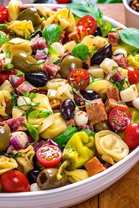 pasta salad with olives, tomatoes, mozzarella and other toppings in a white bowl