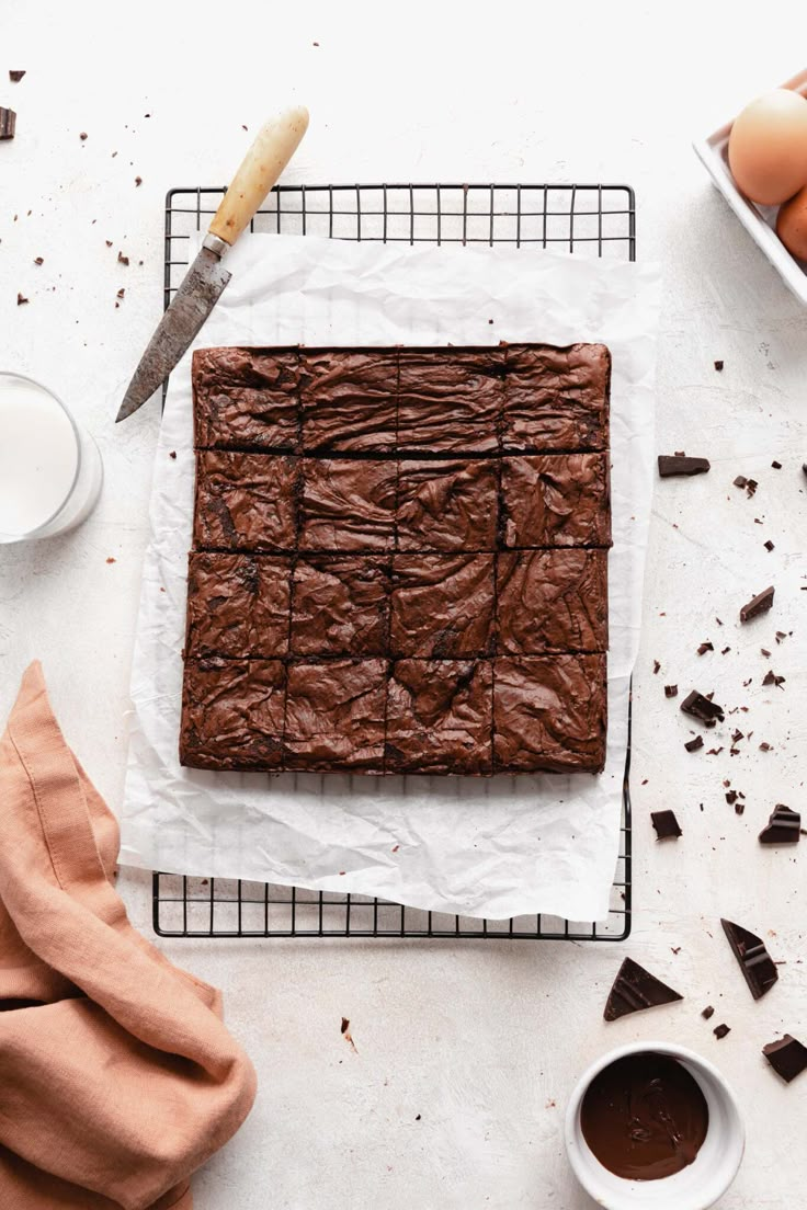 a chocolate brownie sitting on top of a cooling rack next to eggs and milk