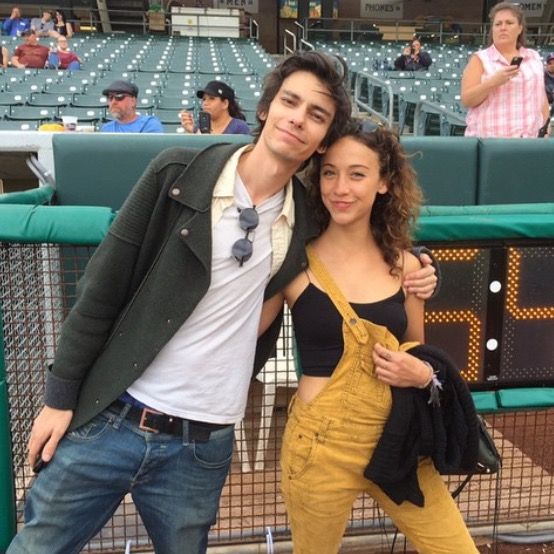 two people standing next to each other in front of a fence at a baseball game