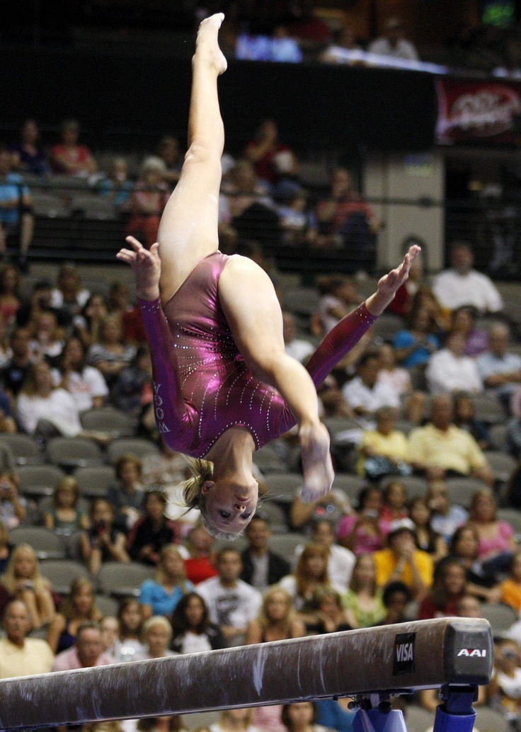 a woman is performing on the balance beam in front of an arena full of people