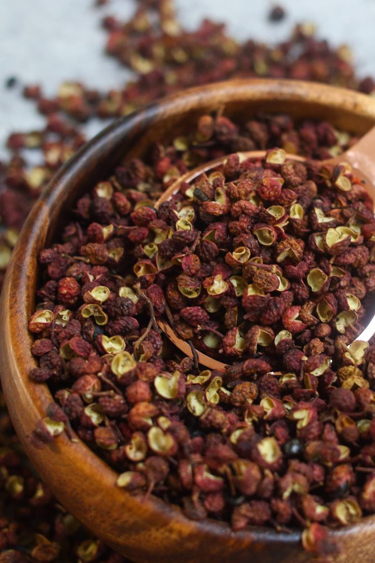 a wooden bowl filled with dried red and yellow flowers on top of a white table