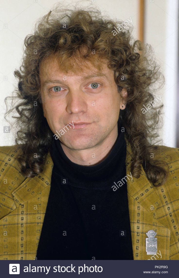 a man with long curly hair wearing a yellow jacket and black turtle neck sweater