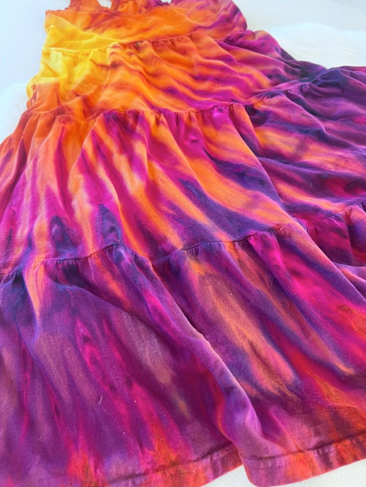 a dress made out of tie dye on a white tablecloth with a pink, orange and yellow design