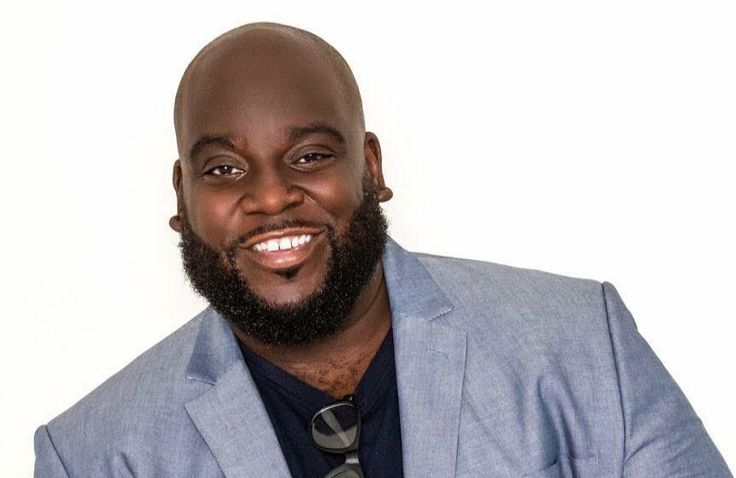 a man with a beard wearing a blue suit and black shirt smiling at the camera