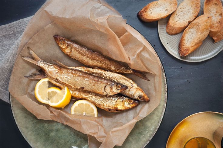 two plates with fish and lemon slices on them next to some toasted baguettes