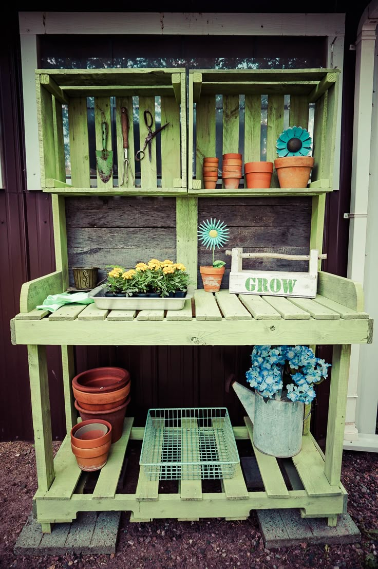 a green shelf filled with potted plants and gardening tools on top of wooden pallets