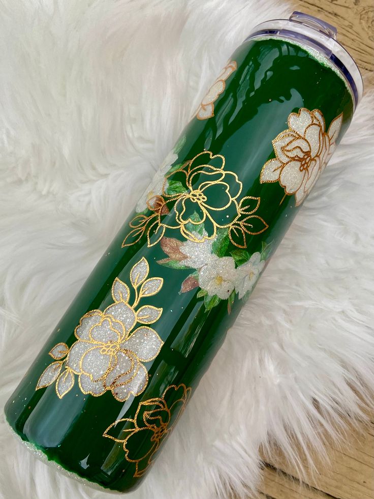 a green tumbler with gold flowers on it sitting on a white furnishing