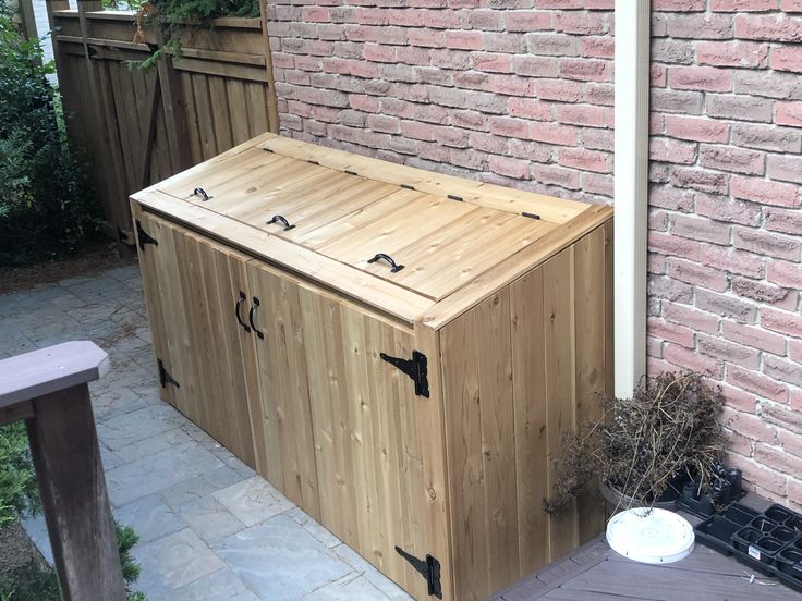 a large wooden storage box sitting next to a brick wall in front of a house