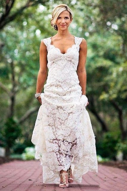 a woman in a white dress is standing on a brick walkway with trees behind her