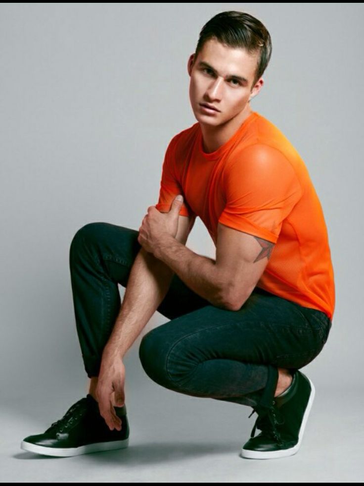 a man in an orange shirt and black pants crouching down with his hands on his knees