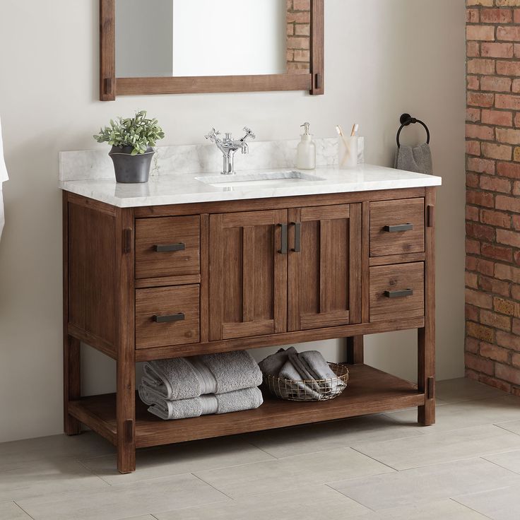 a bathroom vanity with a mirror above it and towels on the floor below, in front of a brick wall