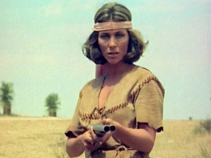 a woman standing in the desert holding a remote control