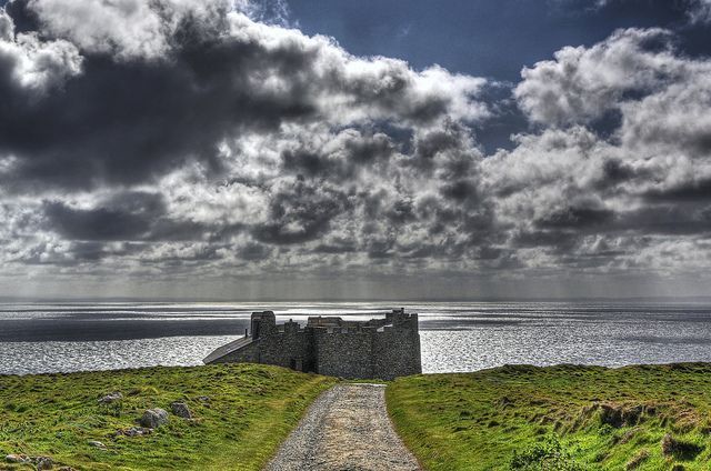 a dirt road leading to a castle on the side of a hill with water in the background