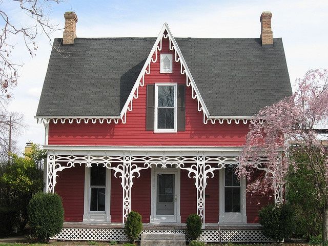 a red house with white trim on the front and side porch, has an arched window