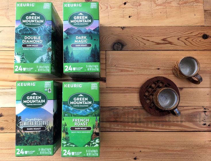 four boxes of green mountain coffee sitting on top of a wooden table next to two cups