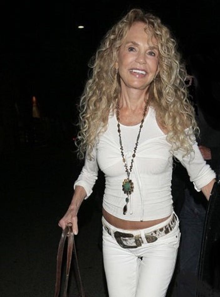 a woman in white is holding a brown purse and smiling at the camera while walking