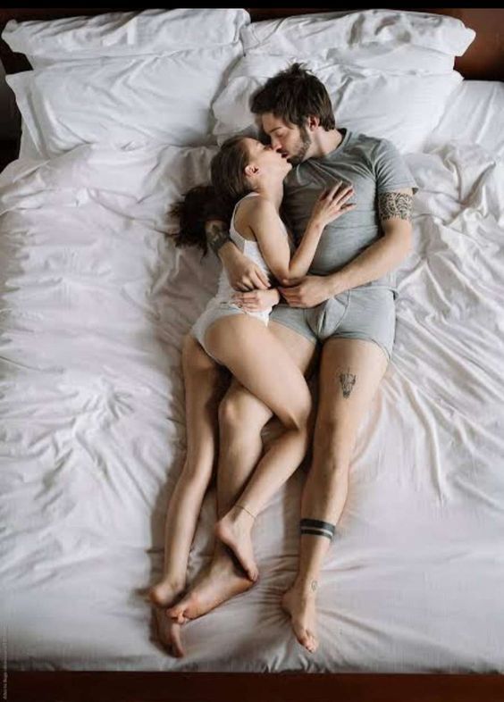 a man and woman laying on top of each other in the middle of a bed