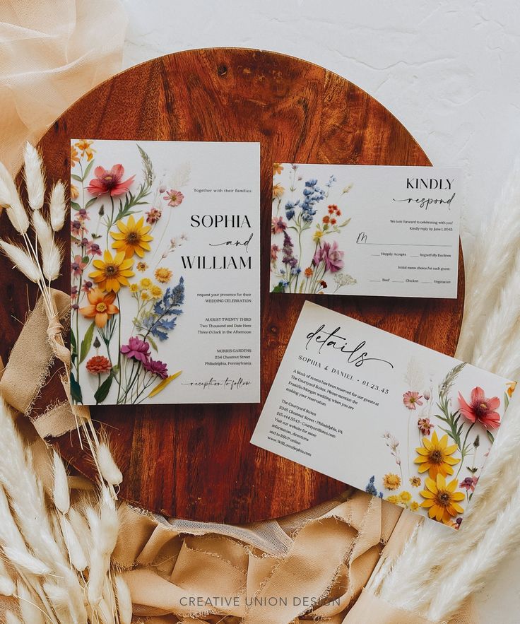 the wedding stationery is laid out on a round wooden table with dried flowers and feathers