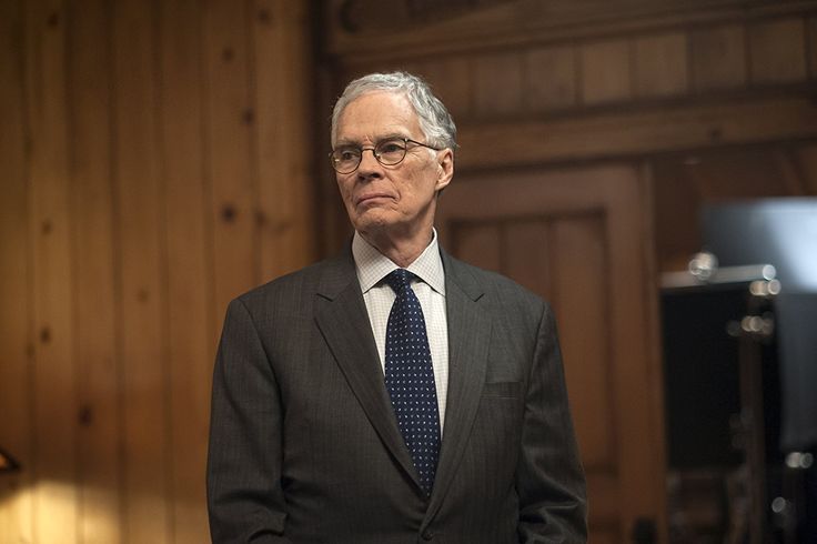 a man in a suit and tie standing in front of a wooden paneled wall