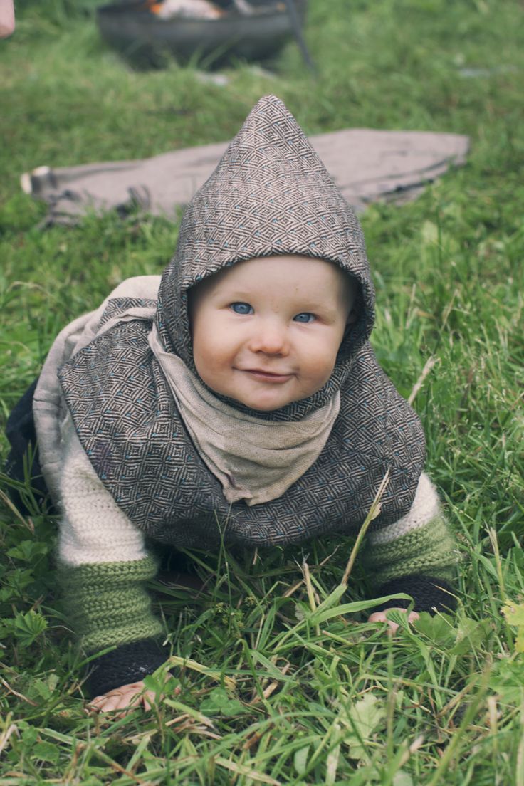 a baby wearing a hat and scarf laying in the grass