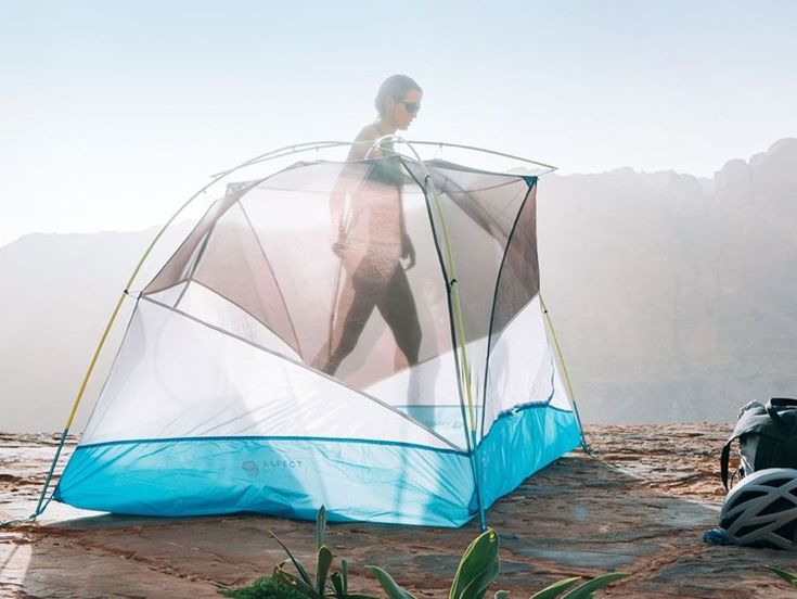 a man standing next to a tent on top of a mountain