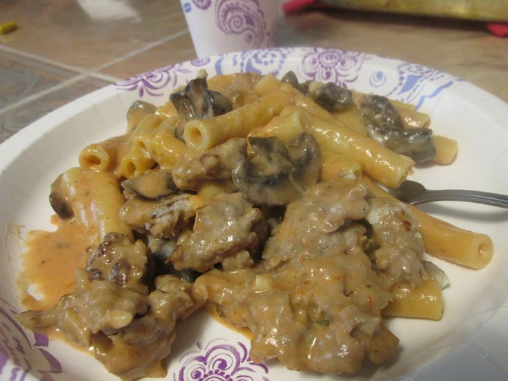 a white plate topped with pasta and meat covered in sauce on top of a table