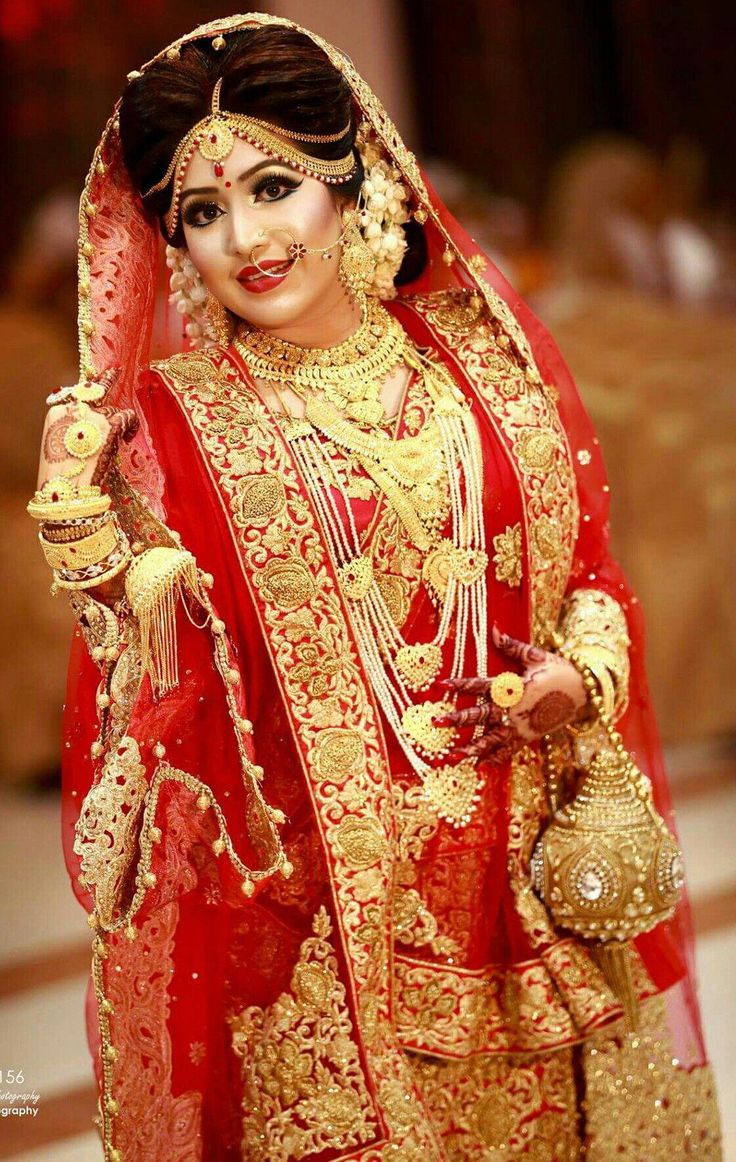 a woman in a red and gold bridal outfit with jewelry on her head, holding a purse