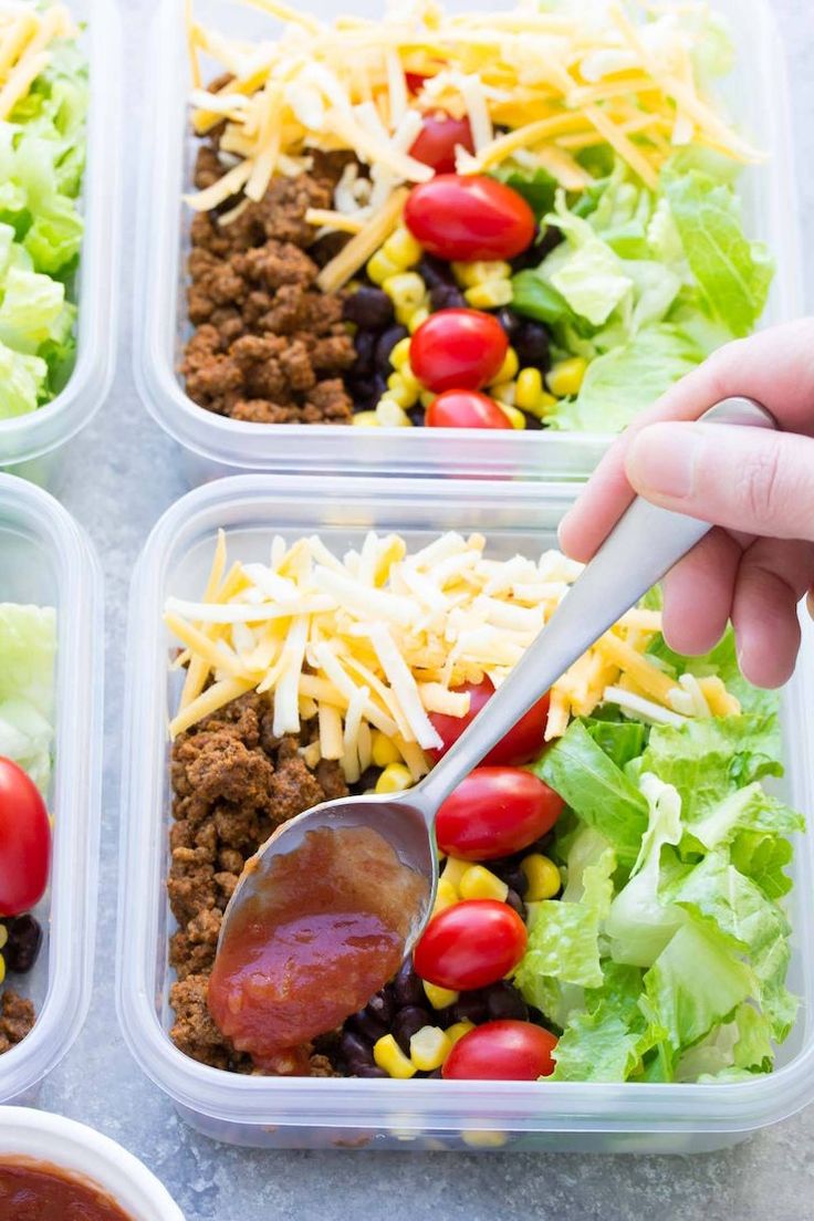 four plastic containers filled with taco salads and lettuce, tomatoes, corn, black beans, cheese