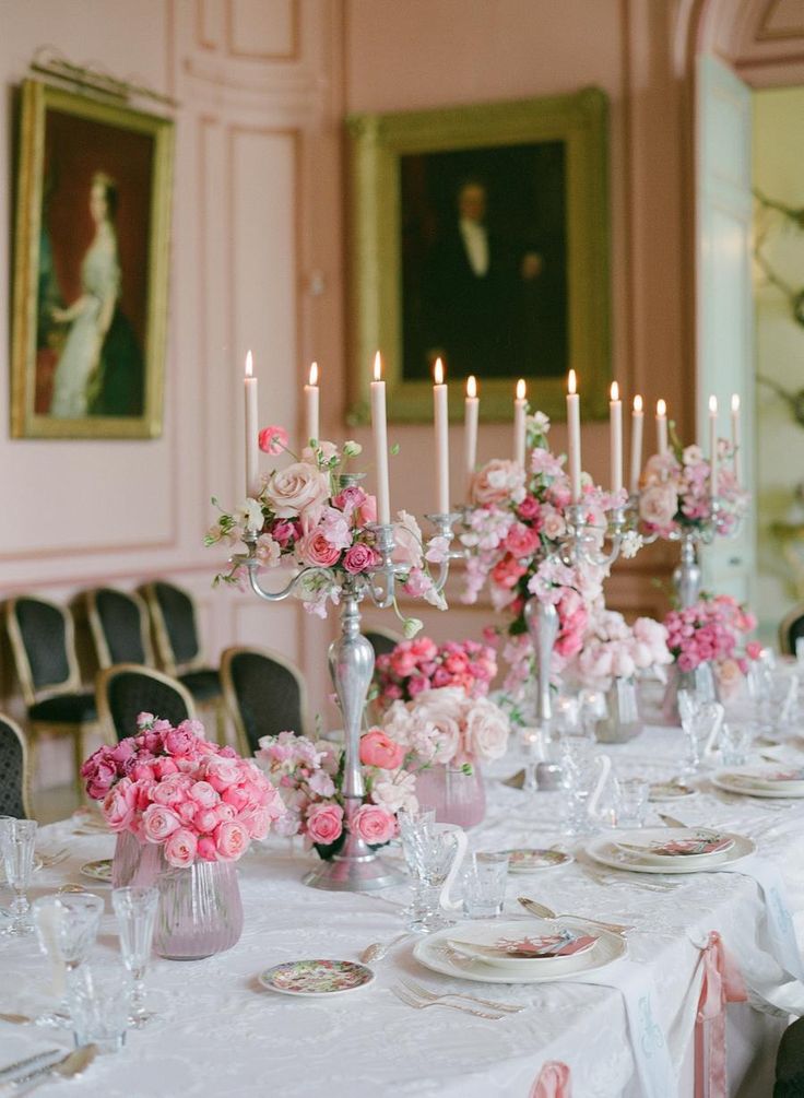 a long table is set with pink flowers and candles for a formal dinner or party