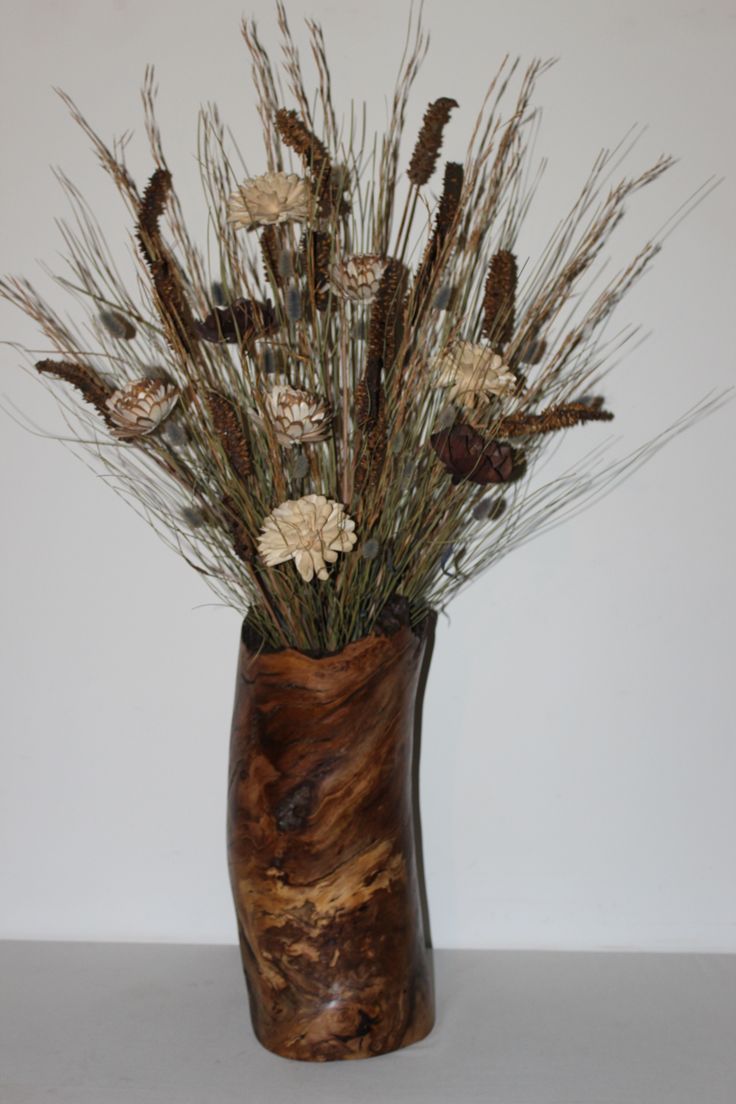 a vase with dried flowers in it sitting on a table next to a white wall