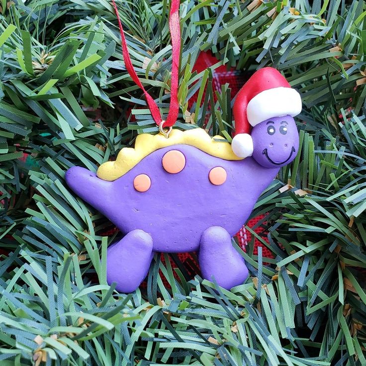 a purple dinosaur ornament with a santa hat on it's head hanging from a christmas tree