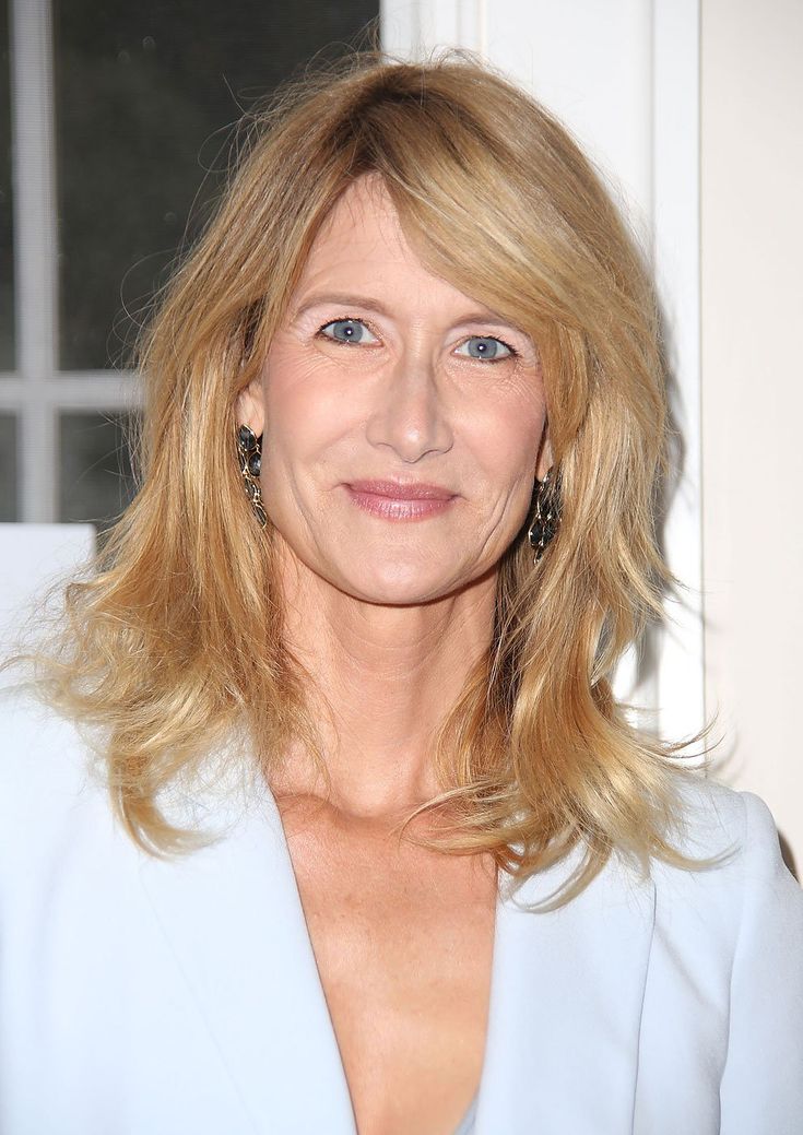 a woman with blonde hair and blue eyes wearing a white suit smiling at the camera