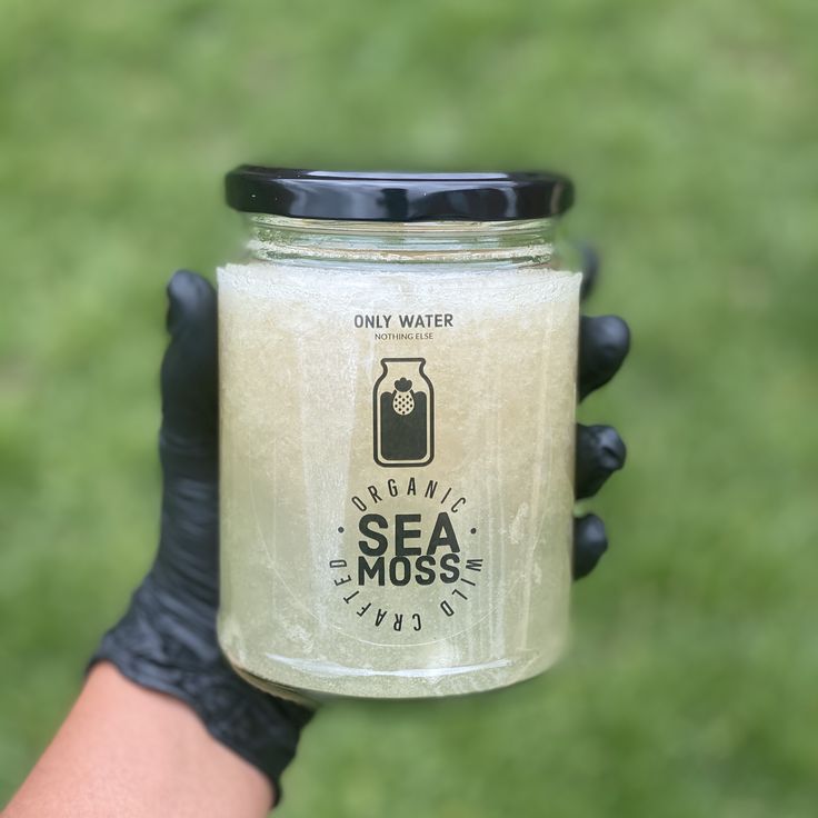 a person holding up a jar with sea moss in it's palm and wearing black rubber gloves