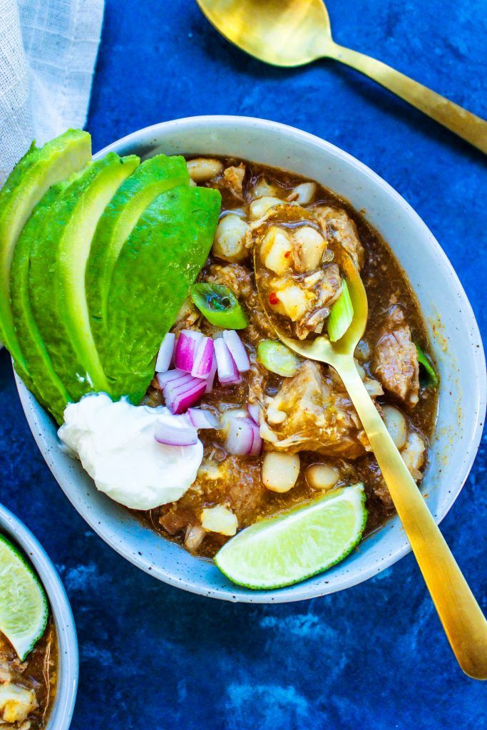 two bowls filled with chili, beans and avocado next to spoons on a blue surface