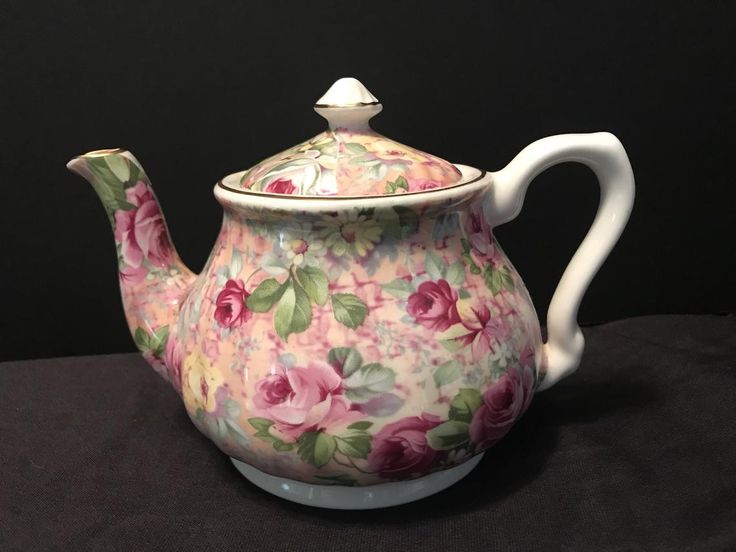 a pink flowered tea pot with a white lid on a black tablecloth background