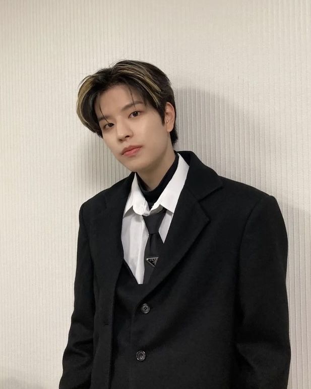 a young man in a suit and tie standing next to a wall with his hands on his hips