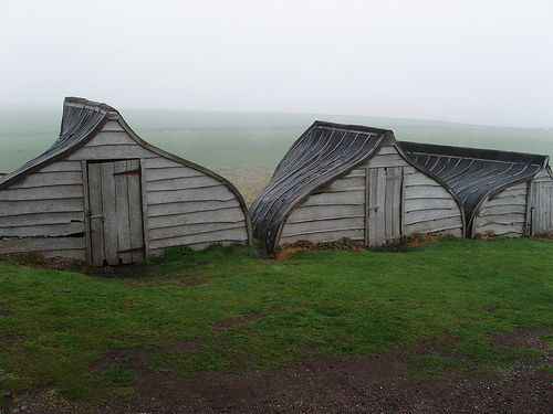 three old wooden buildings sitting on top of a grass covered field next to a body of water