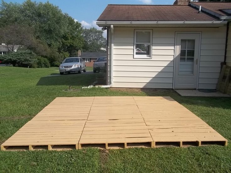 a wooden deck in front of a house with cars parked on the grass next to it