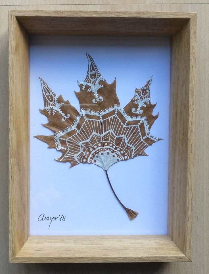 a wooden frame holding a paper cutout of a maple leaf with intricate ...