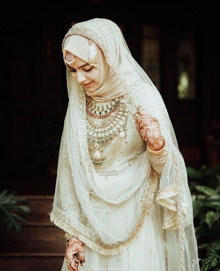 a woman in a white wedding dress and veil with jewelry on her head is walking down some steps