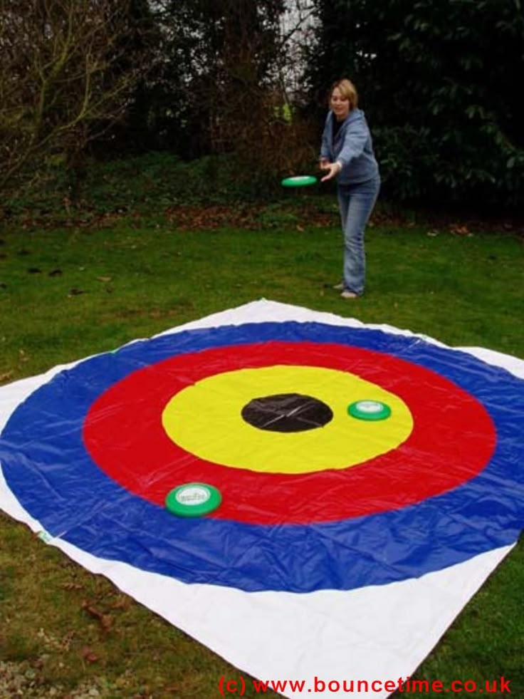 a woman throwing a frisbee on top of a large blanket in the grass