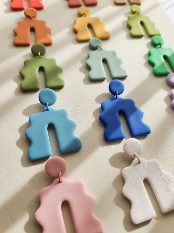 many different colored earrings are arranged on a table with white surface and shadows behind them