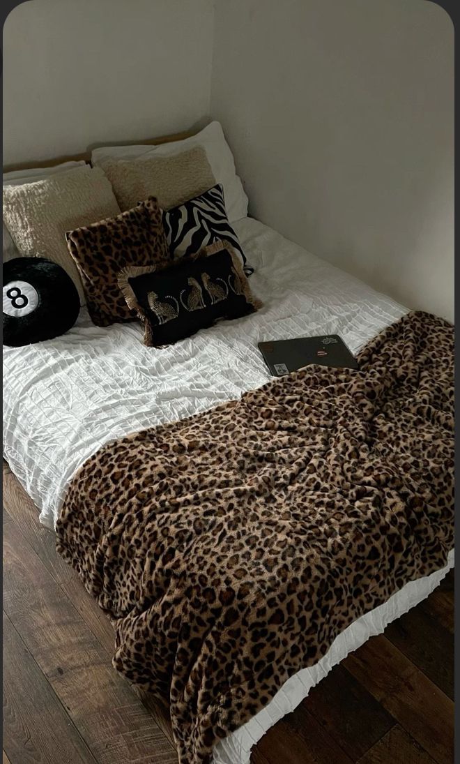 a leopard print comforter on a bed in a room with wood floors and white walls