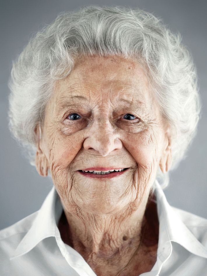 an older woman with white hair and blue eyes smiling at the camera while wearing a white shirt