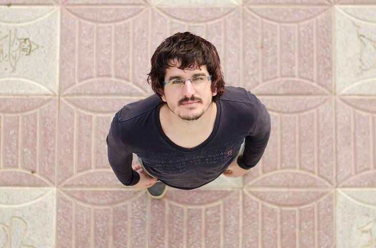 a man with glasses is standing in front of a wall and looking up at the camera