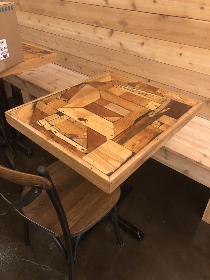 a wooden table with two chairs and a cardboard box on the back wall behind it