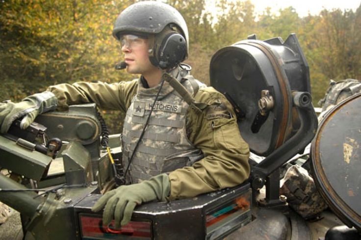 a man sitting in the back of an army vehicle wearing a helmet and goggles