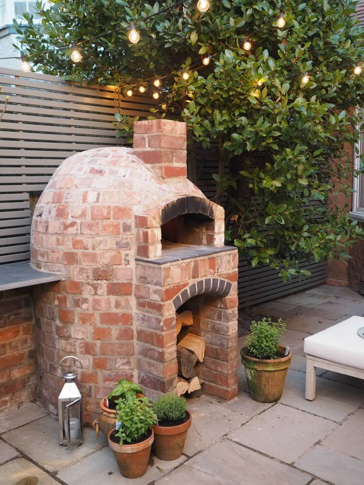 an outdoor brick pizza oven with potted plants and lights on the side of it