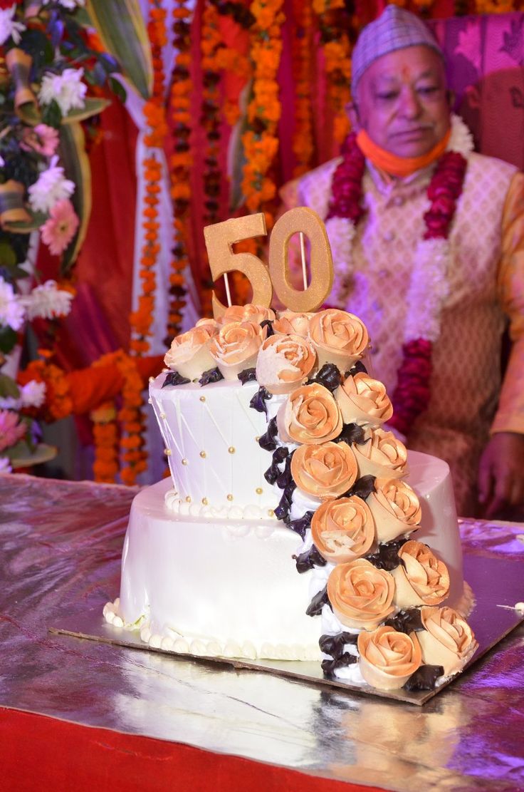 a man standing next to a white cake with flowers on it and the number 50 on top