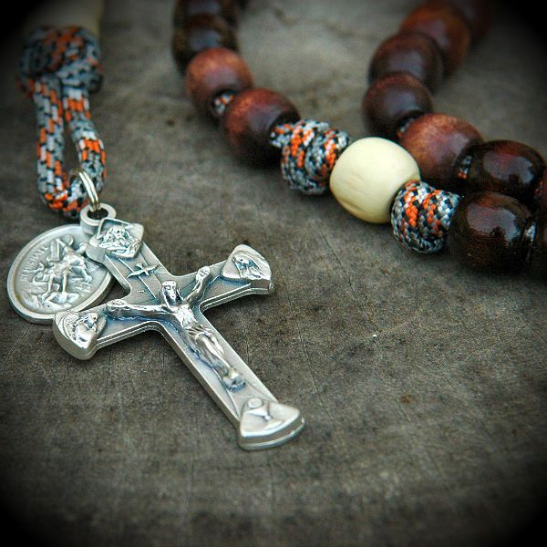 a necklace with a cross and beads on the ground next to it is an orange beaded bracelet